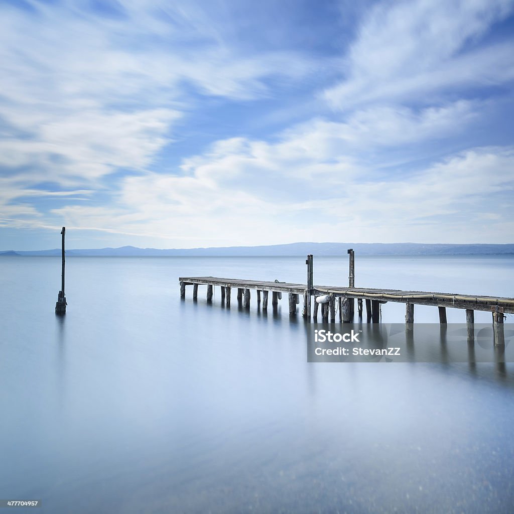 Wooden pier, jetty remains on a blue lake. Long Exposure. Wooden pier or jetty remains on a blue lake sunset. Long Exposure photography Abstract Stock Photo