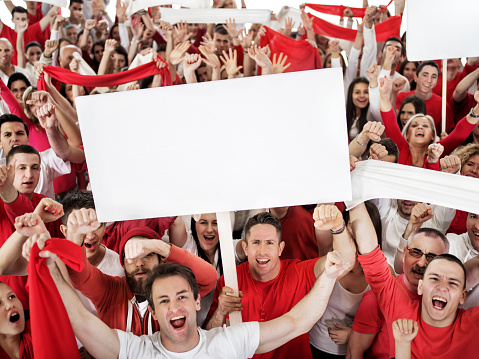 Crowd of cheerful sport fans celebrating with their hands raised and looking at camera. Some of them a re holding banners. Copy space. isolated on white.