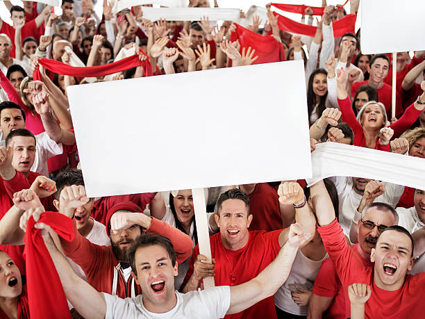 Ecstatic large group of sport fans shouting and cheering. Crowd of cheerful sport fans celebrating with their hands raised and looking at camera. Some of them a re holding banners. Copy space. isolated on white. cheering group of people success looking at camera stock pictures, royalty-free photos & images