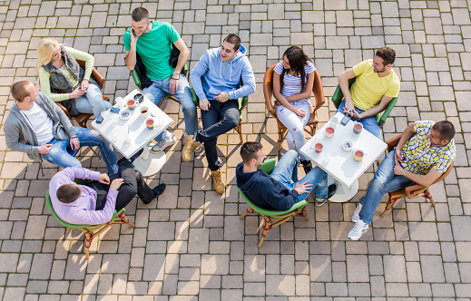 High angle view of group friends sitting in a sidewalk cafe and talking to each other.