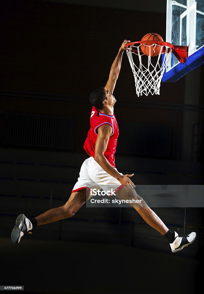 Basketball player slam dunking the ball. Young African American basketball player is jumping and placing the ball in the hoop.   Basketball - Sport Stock Photo