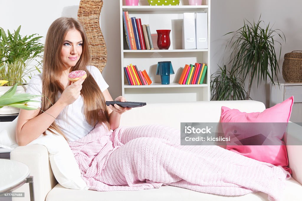 Happy woman watching TV with snack Attractive woman watching TV on the sofa with food Candy Stock Photo