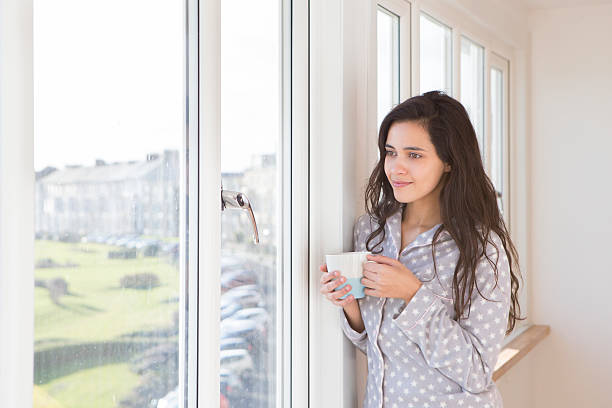 istock Woman Standing by a Window Drinking Coffee in her Pyjamas 477709328