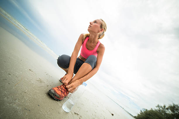 Young woman on the beach on a cloudy day having a break from her morning jogging tying shoes.