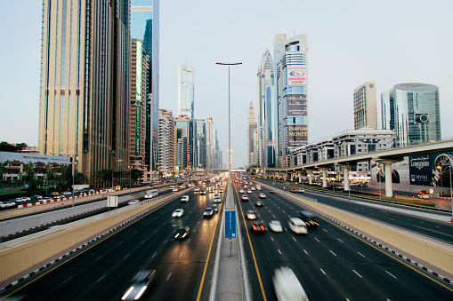 A view of a Dubai multiple lane highway, contemporary architecture in the background.  Skyscrapers,  Dubai cityscape. Clear sky, dusk, nobody, vehicles travelling, horizontal composition. 