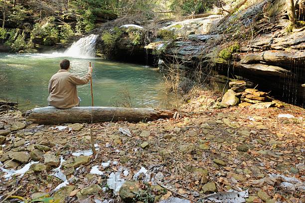 istock Man sitting on log by waterfall 477711707