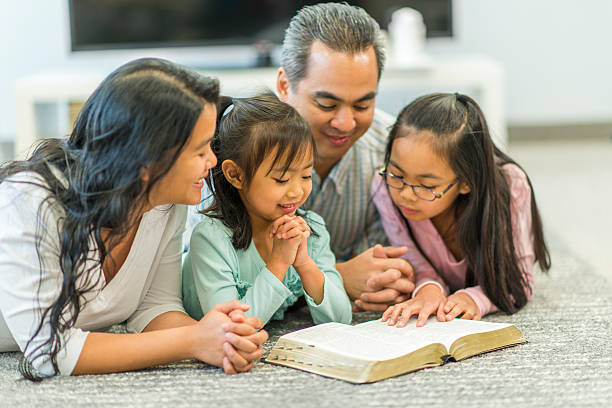 Christian Family Family reading the Bible together in their living room. praying child christianity family stock pictures, royalty-free photos & images