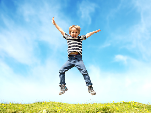 Boy jumping in a meadow at the top of a hill against a blue sky