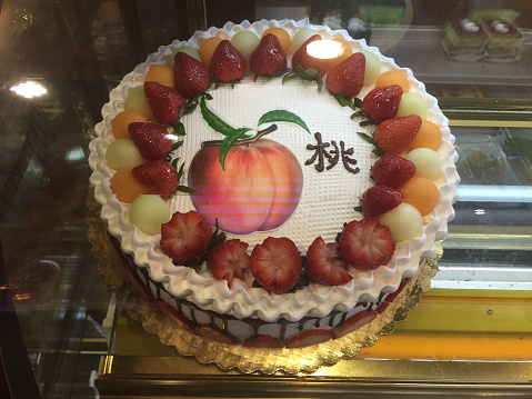 Oriental birthday cake with oriental writing on cake.Plenty of sweets,strawberries,melons,white frosting