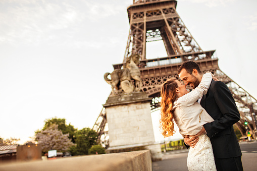 Young married couple is about to kiss in front of an Eiffel tower.