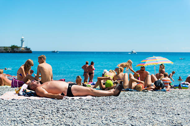 Yalta, Crimea, Ukraine - August 3, 2013: People enjoy a summer day on the beach in the Crimean port of Yalta, in southern Ukraine. The man in the foreground is wearing Adidas swimming briefs and clutching his mobile phone.