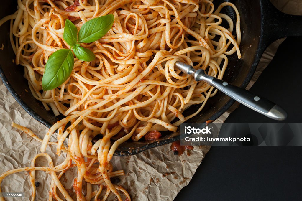 Linguine with Red Sauce and Fresh Basil Linguine with red sauce  and fresh basil sits inside a black cast iron pan on a black surface.  A fork sticks out of the pasta. Linguini Stock Photo