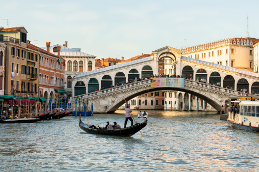 Venice, Italy - May 17, 2012: Gondolier near Rialto bridge, Venice, The Venetian Gondoliere with tourists in gondola at the Canale Grande of Venice. Venice and its Lagoon is an UNESCO World Heritage Site and one of the most visited tourism site in the world. 