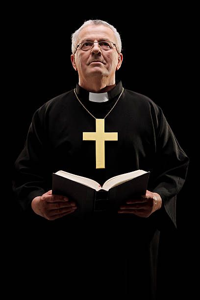 istock Catholic reverend holding a bible isolated on black background 477725643