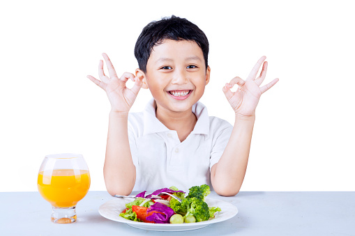 Cute boy making OK gesture while having salad, isolated on white