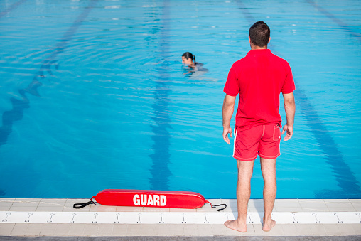 Close-up of a lifeguard's hand grabbing a lifebuoy ring and watching over a swimming pool - Concept of lifeguard at work.