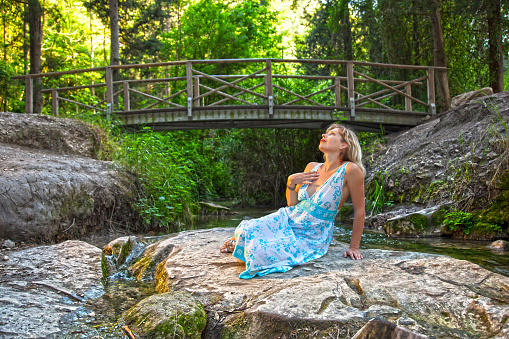 Woman sitting on rocks near bridge across the spring or river