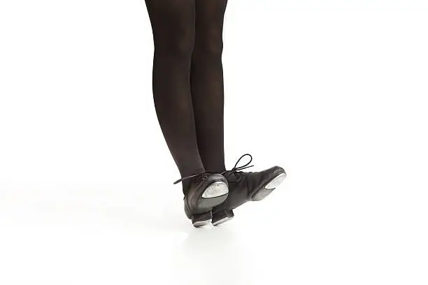 Studio image isolated on white of a young girl's legs in black tights and tap shoes dancing.