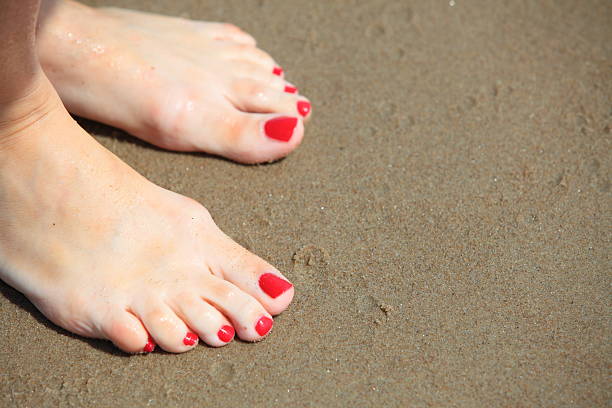 istock Woman feet with red pedicure relaxing on sand 477744021
