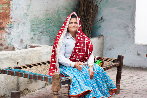 Village Women Sitting on Charpai Near Brick Wall Brick wall wearing Traditional Indian Clothes.