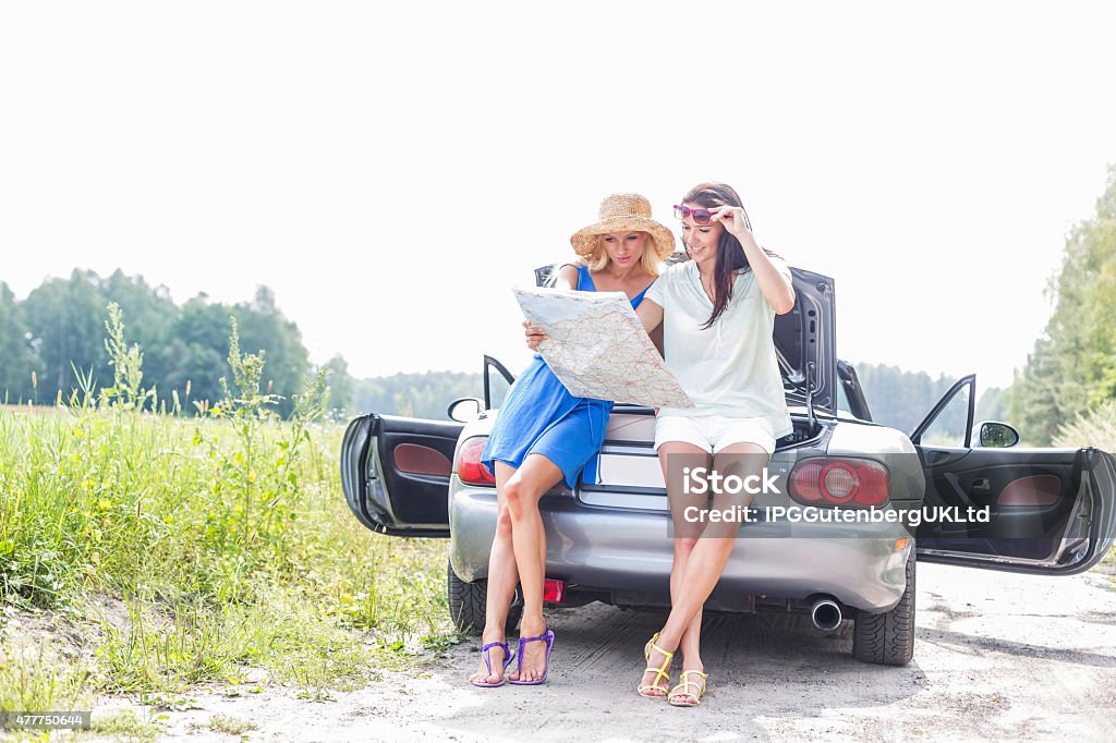 Female Road Trip Female friends reading map while leaning on convertible 20-29 Years Stock Photo