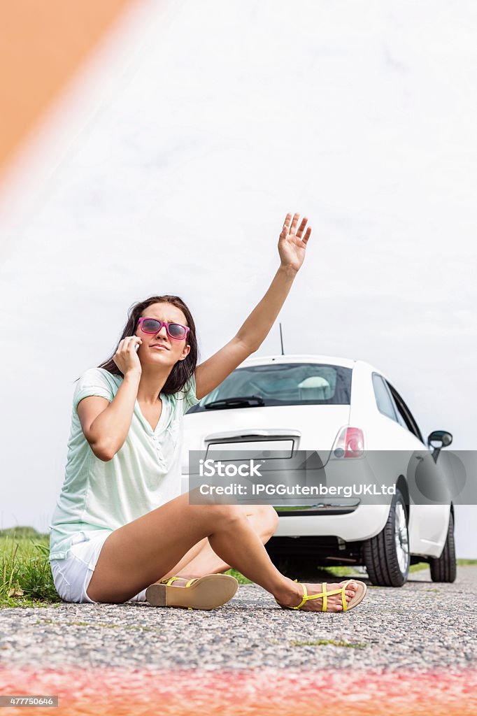 Female Road Trip Frustrated woman hitchhiking while using cell phone on country road by broken down car 20-29 Years Stock Photo