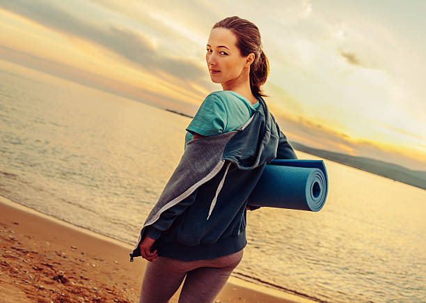 istock Woman with yoga mat standing on beach 477754212