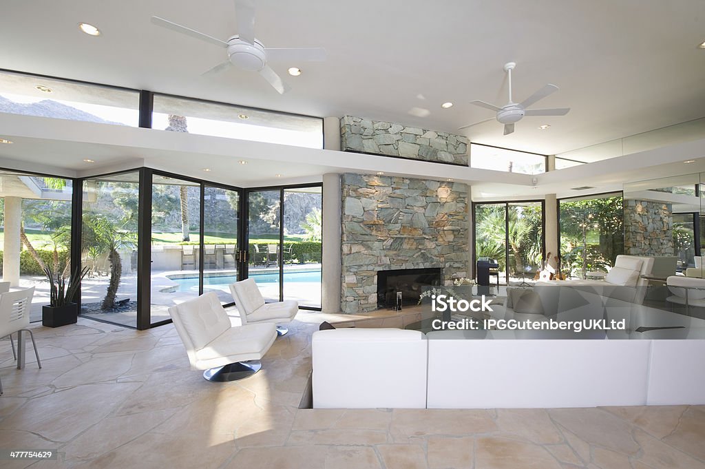 Seating Area And Stone Fireplace In Spacious Living Room Sunken seating area and exposed stone fireplace in spacious living room with view of swimming pool at home Home Interior Stock Photo