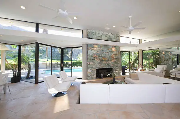 Sunken seating area and exposed stone fireplace in spacious living room with view of swimming pool at home