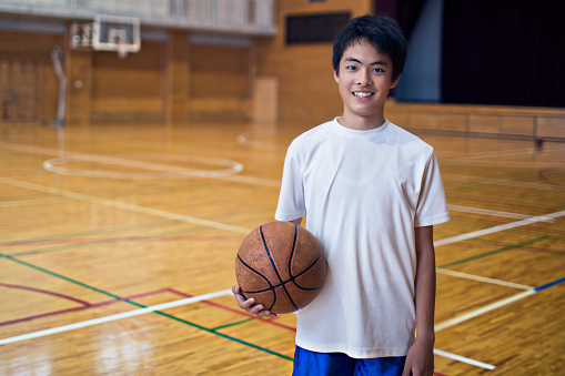 Portrait of a Japanese boy playing basketball in the school gymnasium.