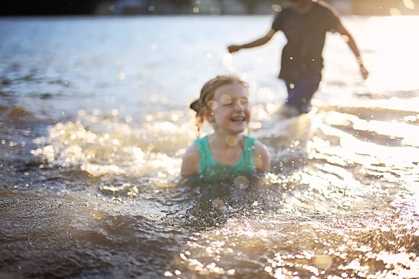 Three children of different age - teenager boy, elementary age girl and toddler girl sitting on a wooden pier by a forest lake looking at camera smiling