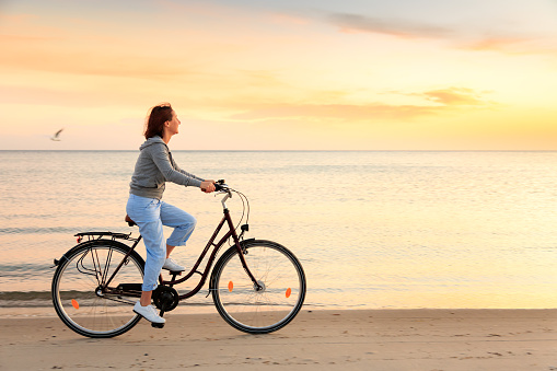 Young caucasian woman riding a bike during sunny day by the sea. Summer vacation concept. Mediterranean islands