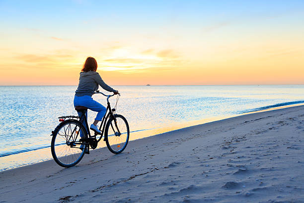 istock Sunset –  woman with bike on beach 477779364