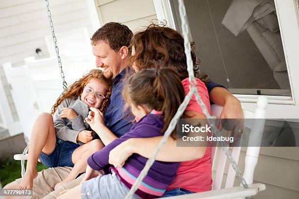 Happy Sisters Sitting With Mom And Dad On Porch Swing Stock Photo - Download Image Now