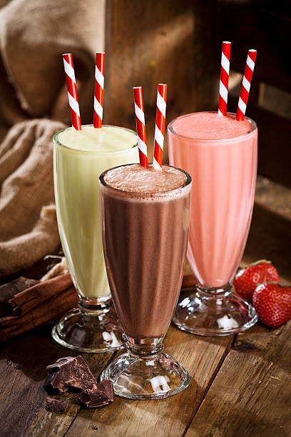 Chocolate, strawberry and vanilla milshakes in rustic wood table Milkshake trio. Chocolate, strawberry and vanilla milkshakes on white table. The glasses are arranged in a triangle with the chocolate milkshake on the foreground while the strawberry milkshake and the vanilla milkshake are in the background. There are two old-fashioned red-and-white straws standing in the glasses. Chocolate chunks, cinnamon sticks and strawberry fruits are at the base of each glass.  DSRL studio photo taken with Canon EOS 5D Mk II and Canon EF 70-200mm f/2.8L IS II USM Telephoto Zoom Lens chocolate shake stock pictures, royalty-free photos & images
