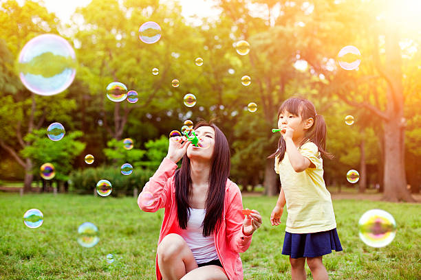 mãe e filha se divertindo no parque com bolhas de sabão - bubble wand bubble child playful - fotografias e filmes do acervo