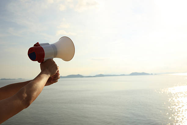 istock hands hold megaphone with sea under blue sky background 477816534