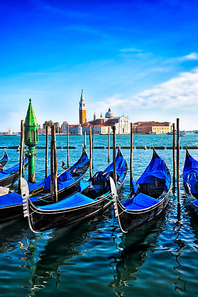 View of the iconic Venice gondolas in Italy. Viewed from Piazza San Marco (St Mark's Square). The church of San Giorgio Maggiore is visible in the background. Dramatic sunset cloudscape over the blue water.