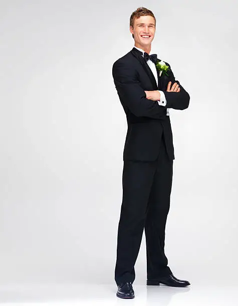 Attractive young groom smiling while in his tuxedo and isolated on white - portrait
