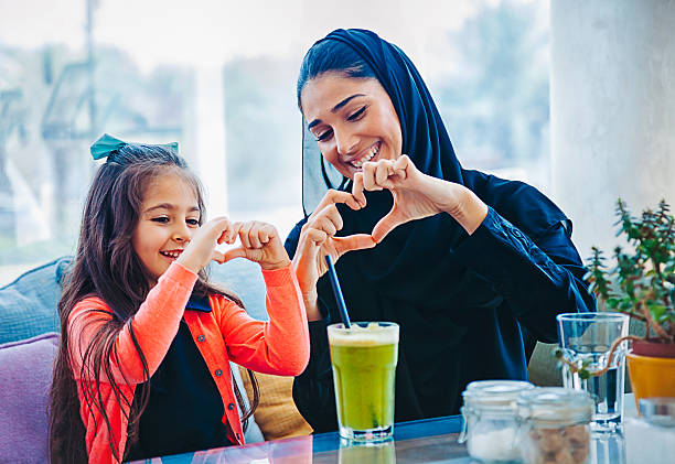 Heart shape made with hands Middle eastern beautiful mother and cute daughter showing forming heart shape symbol making with their fingers hands and smiling at cafe restaurant middle eastern culture stock pictures, royalty-free photos & images
