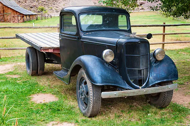 Photo of an antique black pickup Ford at a farm. A barn on background.