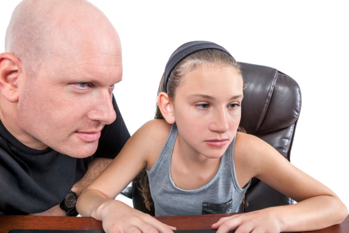 A father and his daughter both stare intently at a computer screen that cannot be seen.  rr