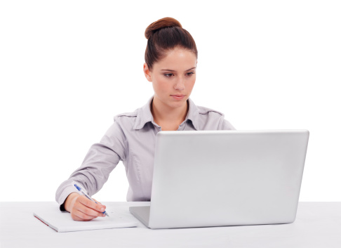 Shot of a young woman seated in front of a laptop and taking notes isolated on white