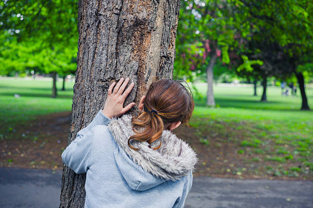 istock Woman hiding behind tree in park 477844198