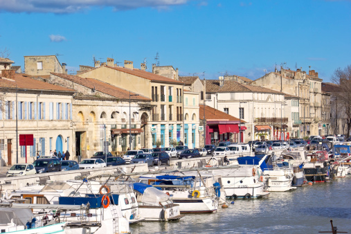 Beaucaire, France - March 4, 2014: View to the harbor of Beaucaire, to the ships and boats. In background are seen some people, cars and typical buildings of the Provence (South of France. The harbor is part of a Rhone Canal. Beaucaire is a very amazing place in the Gard department in Languedoc-Roussillon in southern France. Beaucaire is located on the Rhône River, opposite the town of Tarascon, which is in Bouches-du-Rhône department of Provence.