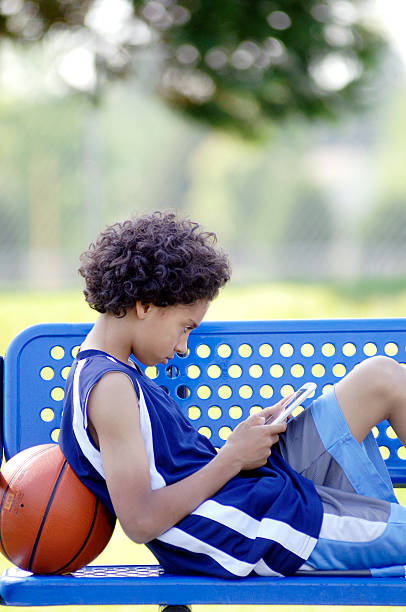African American Boy reading a mobile tablet in the park stock photo