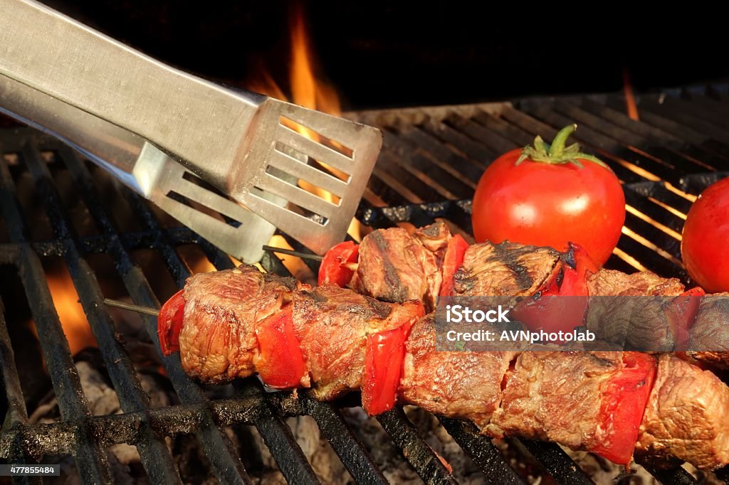 Tongue Hold BBQ Beef Shish Kebab On The Hot Grill Tongue Hold BBQ Beef Shish Kebab With Vegetables On The Hot  Flaming Cast Iron Grill Close-up 2015 Stock Photo