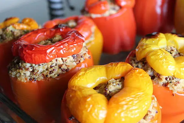 This image shows a few stuffed bell peppers (stuffed with quinoa, onions, chicken, almonds, spices, etc.), after baking. The image was staged to emulate a domestic or commercial kitchen and service environment. 