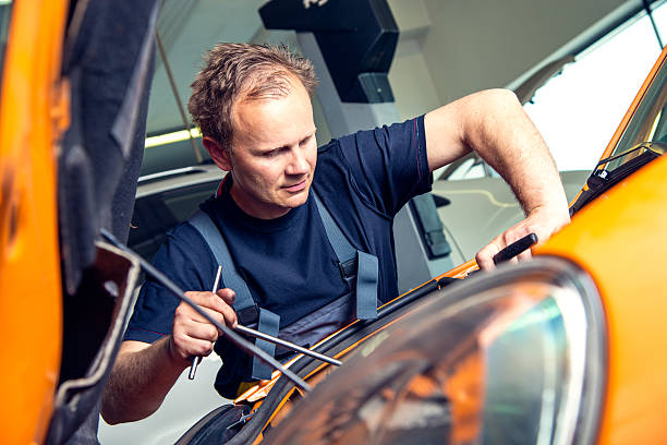 istock Male Mechanic Peering into Engine Compartment of Car 477861069
