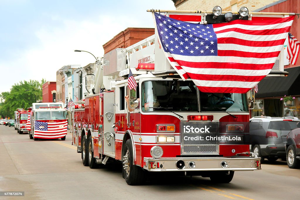 Fire Trucks with American Flags at Small Town Parade A group of fire trucks with American flags on them drive down the road in a small town American Parade during a festival event. Parade Stock Photo